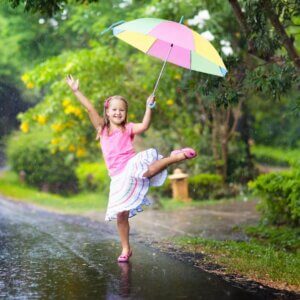 Young girl holding a colorful umbrella while dancing in the rain. 